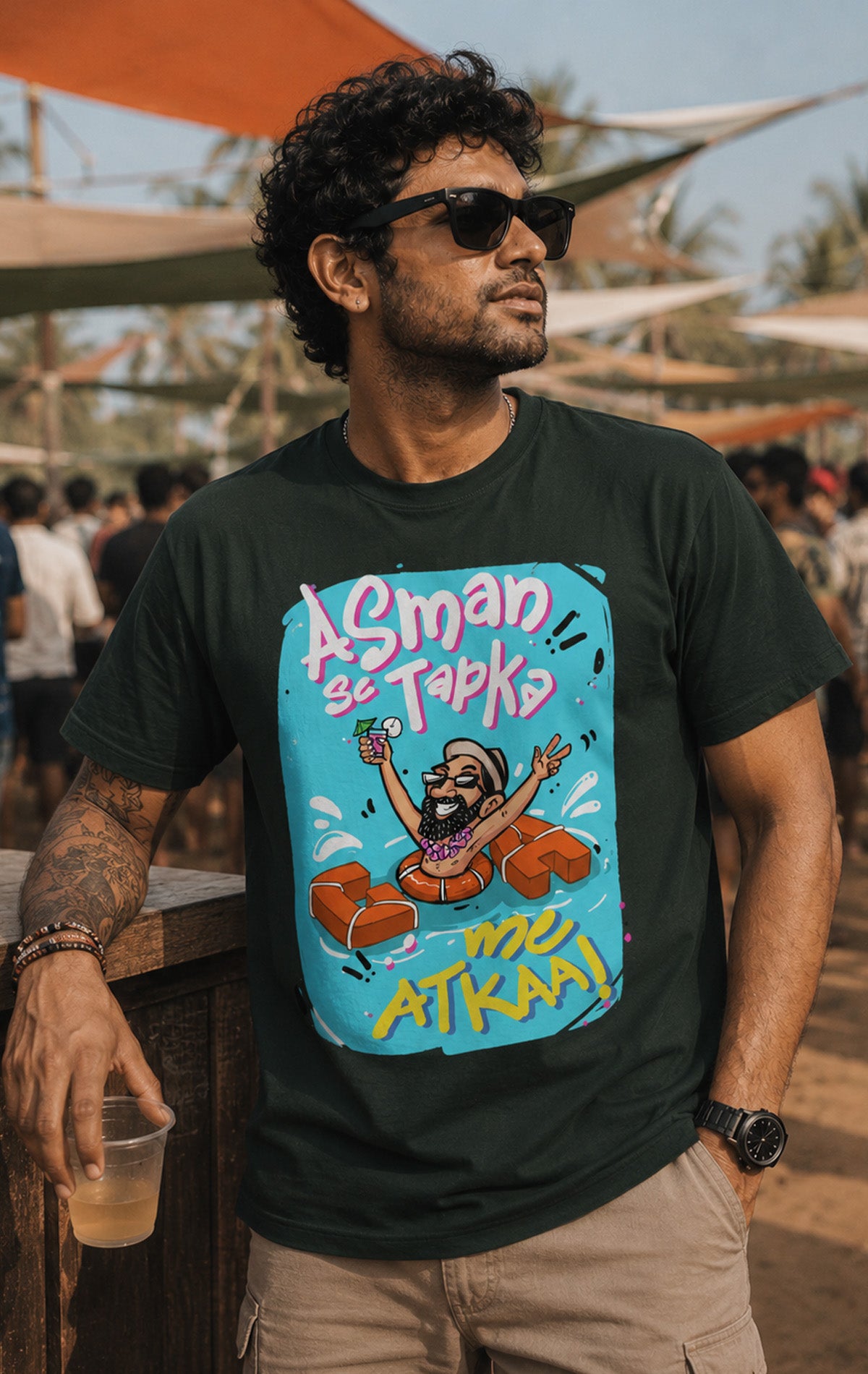 A man smiling on a sunny beach wearing a steel grey Oi Patrao t-shirt with the funny Hindi phrase Asman se Tapka Goa me Atkaa