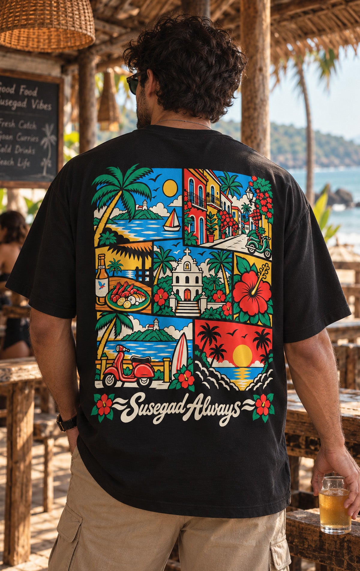 Man wearing black oversized Susegad Always t-shirt with colourful Goa beach, church, houses and seafood back print, Oi Patrao