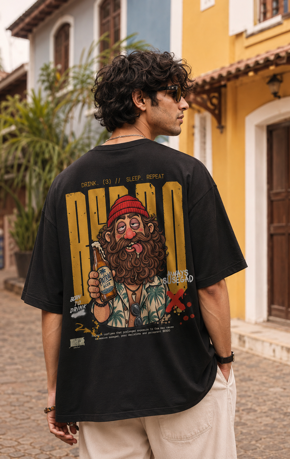 Black oversized t-shirt back print featuring illustrated Goan character holding a beer bottle with Bebdo typography, funny Goa t-shirt